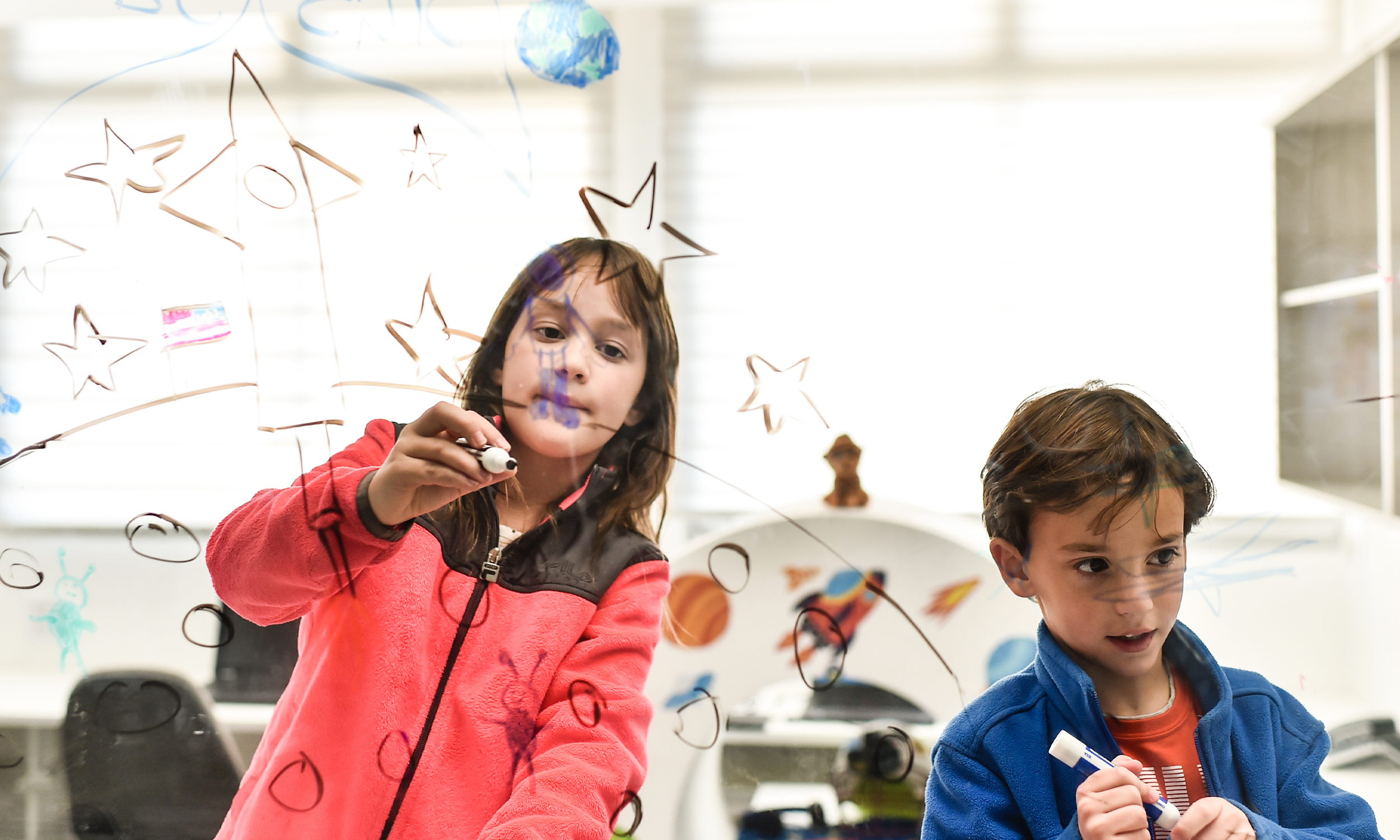 Young girl and boy drawing stars and a rocket on a clear glass window